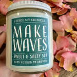 Jar candle labeled "Make Waves" surrounded by pink flower petals