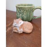 Small fox figurine in front of a green ceramic mug