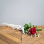 Single red rose with small white flowers in a paper wrap