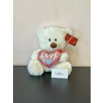 White teddy bear holding a pink heart pillow with a red tag