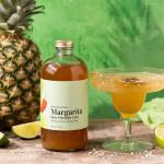 Bottle of margarita mixer beside a margarita glass and pineapple
