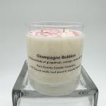 White soy wax candle labeled Champagne Bubbles in a clear glass jar on a glass stand