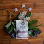 Tea bags and sprigs of greenery arranged on a wooden surface
