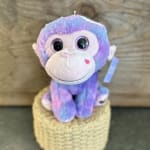 Pastel plush monkey toy with glittery eyes sitting on a woven basket