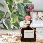 A reed diffuser bottle with dried pink flowers in a clear tube