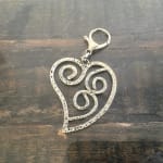 Silver heart-shaped keychain charm with spiral cutouts on a dark wooden surface