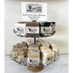Two-tiered wire stand displaying assorted goat's milk soap bars with beige labels.