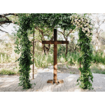 Wooden cross under a floral arch with white flowers and greenery