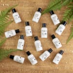 Assorted lotion bottles arranged on a woven mat with fern fronds