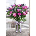 Pink roses and carnations in a clear glass vase with a lavender ribbon