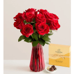 Red roses in a red glass vase with a box of chocolates beside them