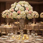 Tall centerpiece of white hydrangeas and blush roses in a clear glass vase