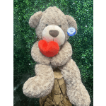 Large plush teddy bear holding a red heart against a green wall