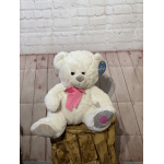 White teddy bear with a pink ribbon sitting on a wooden stump