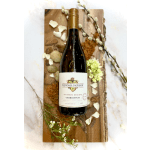 Bottle of white wine on a wooden board with scattered white petals and small blossoms.