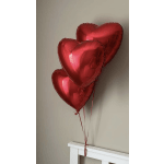 Three red heart-shaped balloons tied together above a white bed frame
