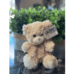 Plush teddy bear with a pink polka-dot bow sitting in front of greenery