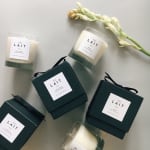 Assorted white candles in glass jars with dark green gift boxes and a white flower stem