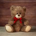 Brown teddy bear with a red bow sitting against a wooden background