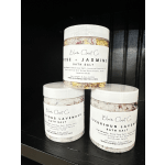 Three jars of floral bath salt with white lids on a dark shelf