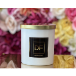 White candle tin with gold lid in front of blurred flowers