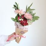 Handheld bouquet of pink and red flowers wrapped in paper with a ribbon