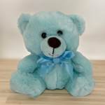 Light blue teddy bear with a ribbon bow sitting on a wooden surface
