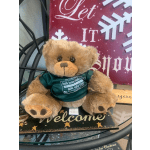 Teddy bear in a green shirt sitting on a holiday sign