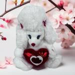 White plush teddy bear holding a red heart in front of pink blossoms