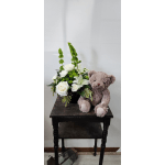 White floral arrangement with a teddy bear on a table