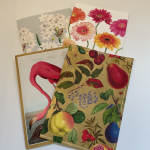 Four decorative floral and fruit-themed cards are stacked on a white surface.