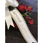 Sympathy spray with red flowers and a white ribbon reading Beloved Father, accented by a large ivory bow.