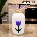 Potted air plant in a white vase with a purple tulip design