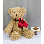 Tan plush teddy bear with a red satin bow sitting beside a florist card