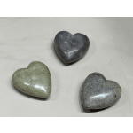 Three polished stone heart keepsakes in gray and green tones on a light surface