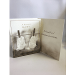A baby congratulations card with white booties clipped on a line