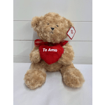 Tan teddy bear holding a red heart with the words "Te Amo" on a white surface
