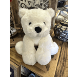 White plush teddy bear sitting on a wooden shelf