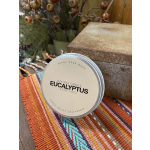 A tin candle labeled eucalyptus sits on a colorful woven cloth.