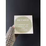 Hand holding a square retirement sign with green text on a white background