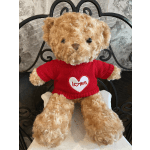 Tan teddy bear in a red heart sweater seated against a decorative metal backing