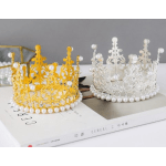 Two decorative pearl crowns, one gold and one silver, sit on a book.
