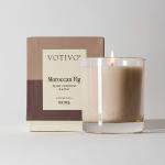 Lit glass candle beside its box labeled Moroccan Fig