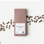 Dark chocolate espresso bar in mauve wrapper with coffee beans scattered on a white surface