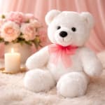 White teddy bear with a pink bow beside a candle and blush flowers
