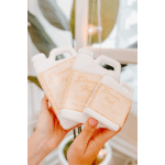 Hands holding three white bottles with peach labels.
