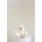 Cream teddy bear with a ribbon sitting on a white pedestal