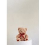 Plush teddy bear with a red heart ribbon sitting on a white pedestal