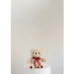Plush teddy bear with a red ribbon sitting on a white pedestal
