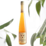 A tall bottle of honey with a label, framed by blurred green leaves.